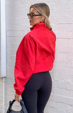 Side view of a red funnel neck sports jacket with raglan sleeves and elasticated cuffs