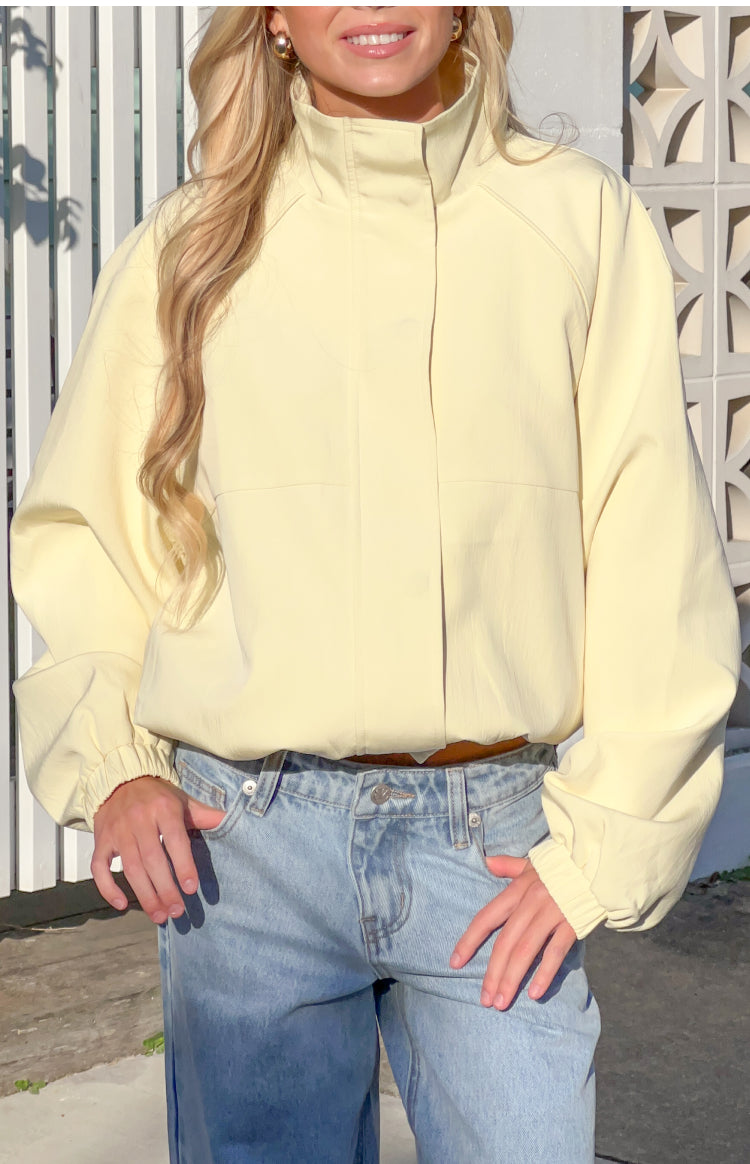 Front view of a yellow funnel neck sports jacket with a hidden placket and voluminous long sleeves with elasticated cuffs