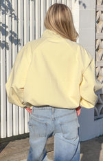 Rear view of a yellow funnel neck sports jacket with raglan sleeves and an elasticated hem