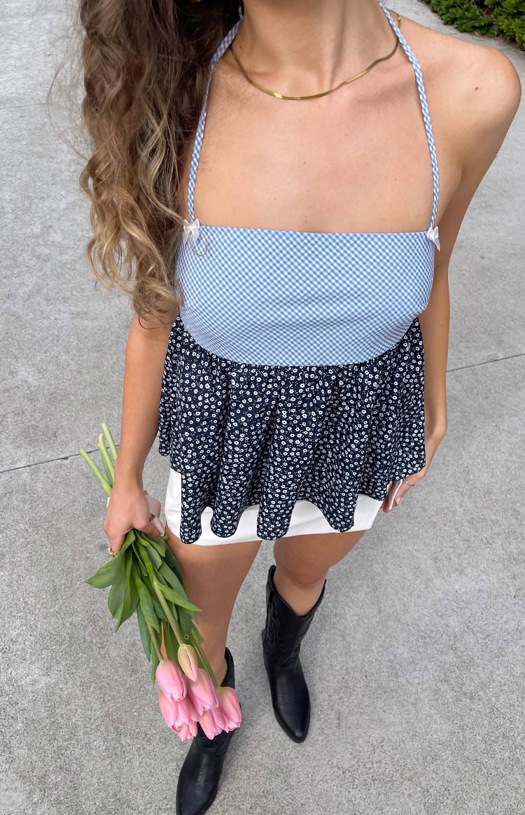 Overhead view of a blue gingham bandeau halter top with braided straps, small white bows, and a dark floral peplum hem