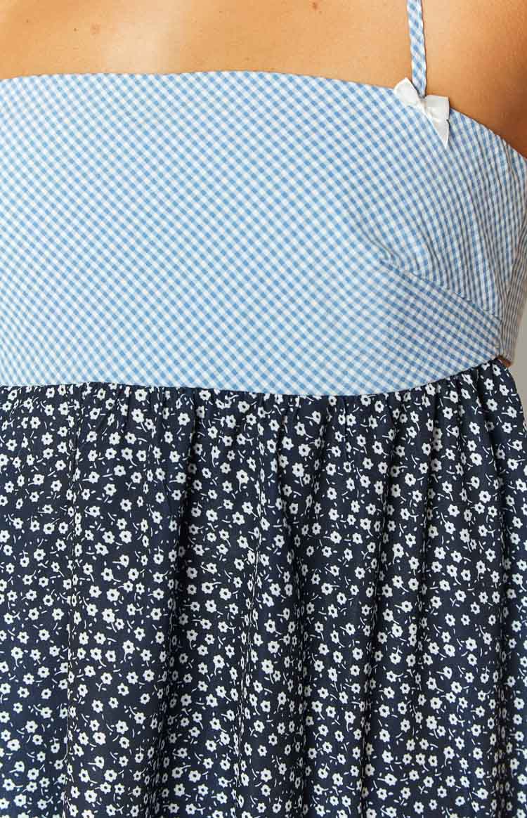 Close-up of the light blue gingham pattern bodice with a white bow on the strap, meeting a gathered navy floral print