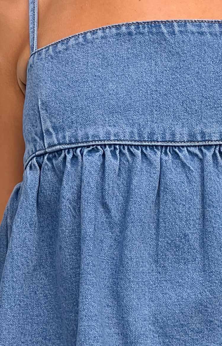 Close-up of the gathered waist seam detail on the blue denim top, highlighting the fabric texture