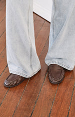 Close-up of brown slip on loafers featuring a penny strap and detailed moc toe stitching