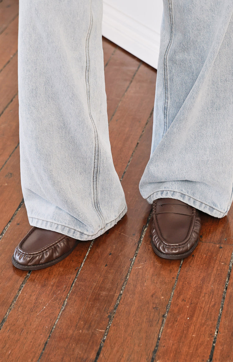 Close-up of brown slip on loafers featuring a penny strap and detailed moc toe stitching