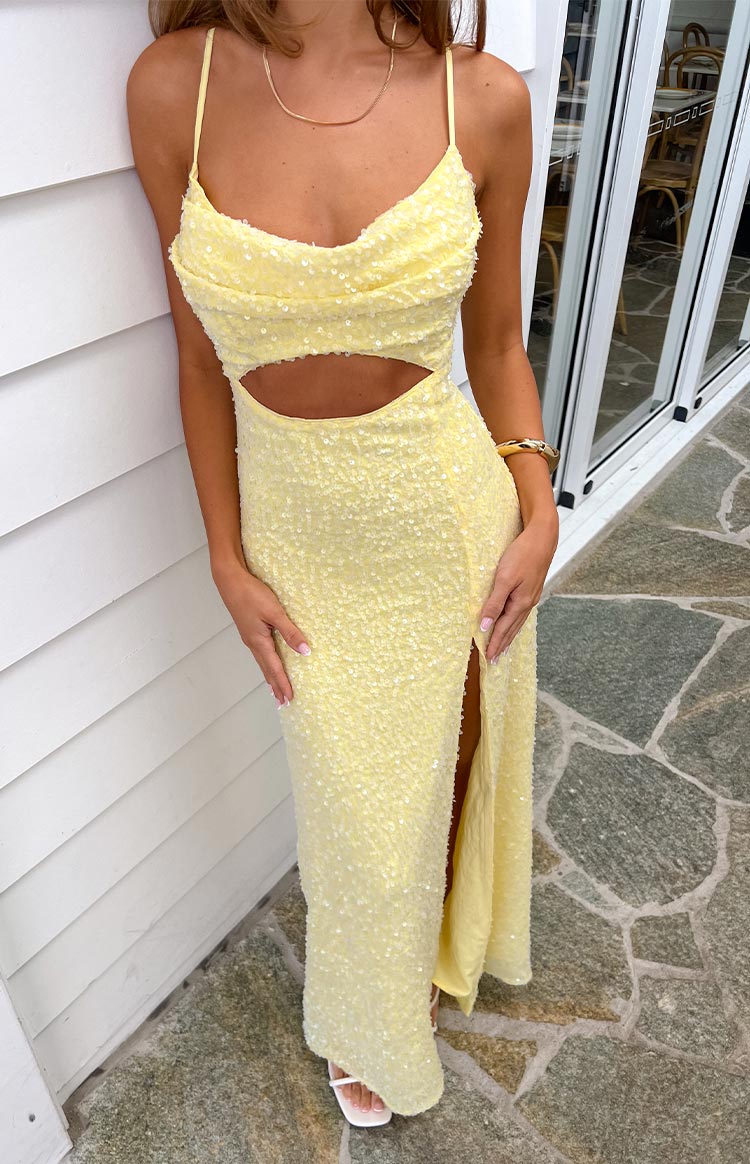 A shimmering pale yellow maxi dress with delicate spaghetti straps- a cowl neckline- a midriff cutout- and a high side slit- detailed with subtle sequins throughout.