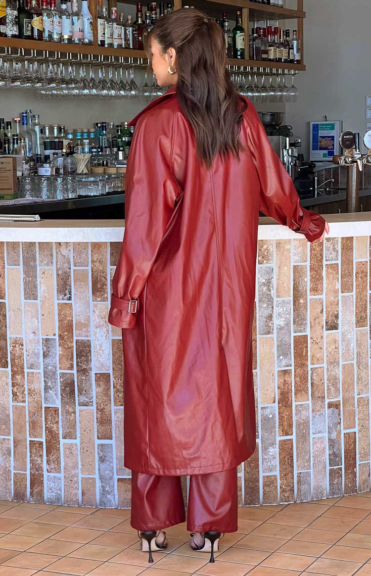 Back view of the long, relaxed fit red PU trench coat with buckle details on the sleeve cuffs