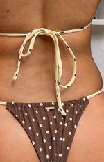 Close-up of the back tie detail of brown polka dot bikini bottoms, showing the cream tie with brown dots and ruched top edge