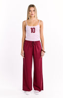 The back view of a pair of dark red wide-leg sweatpants with an elastic waistband featuring a large white number 10 graphic on the left hip.