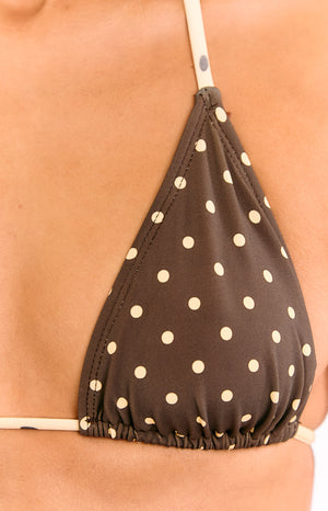 A close-up view of our model showing a brown triangle bikini top with a small white polka dot pattern and a light-colored strap with small black polka dots.