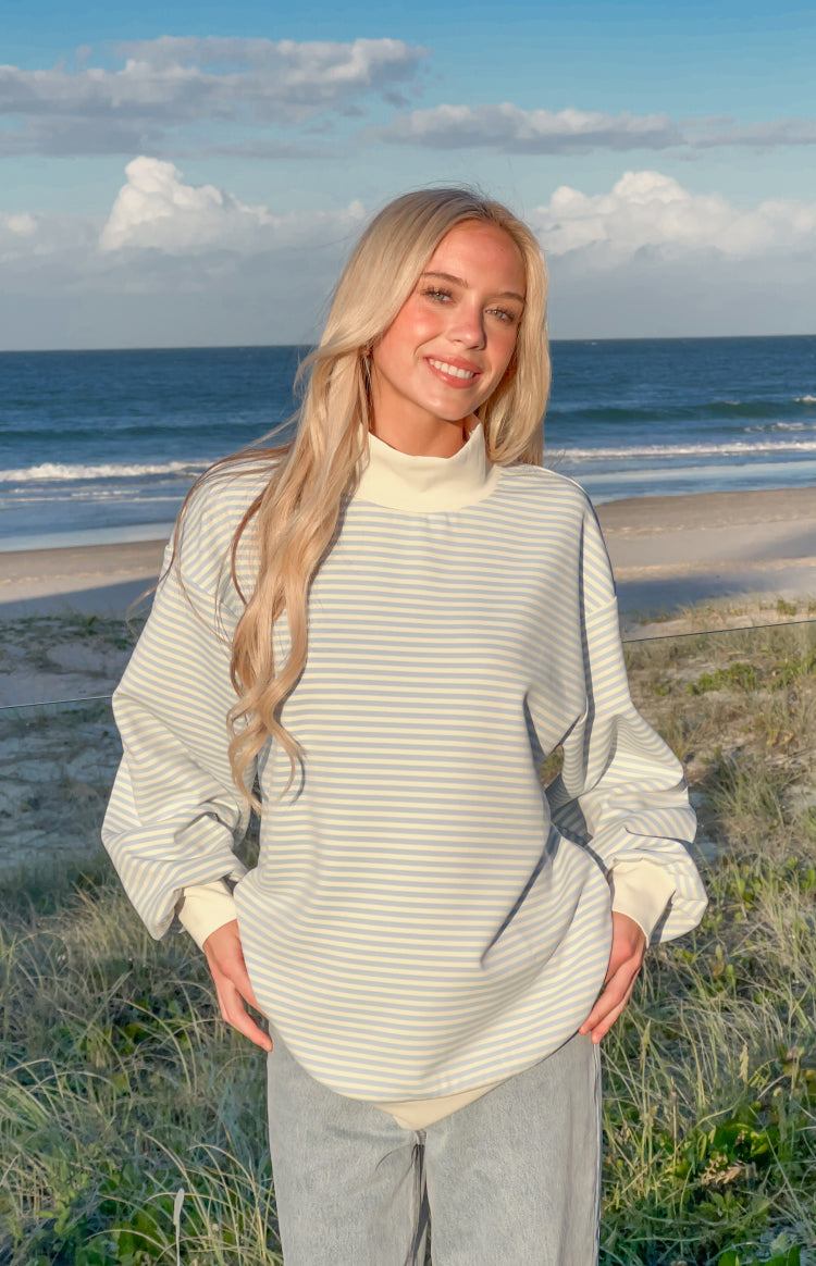 Front view of a blue and cream horizontal stripe mock neck sweater with oversized fit and cream ribbed cuffs