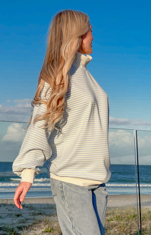 Side view of a blue and white striped mock neck sweater with long balloon sleeves and cream ribbed cuffs and hem