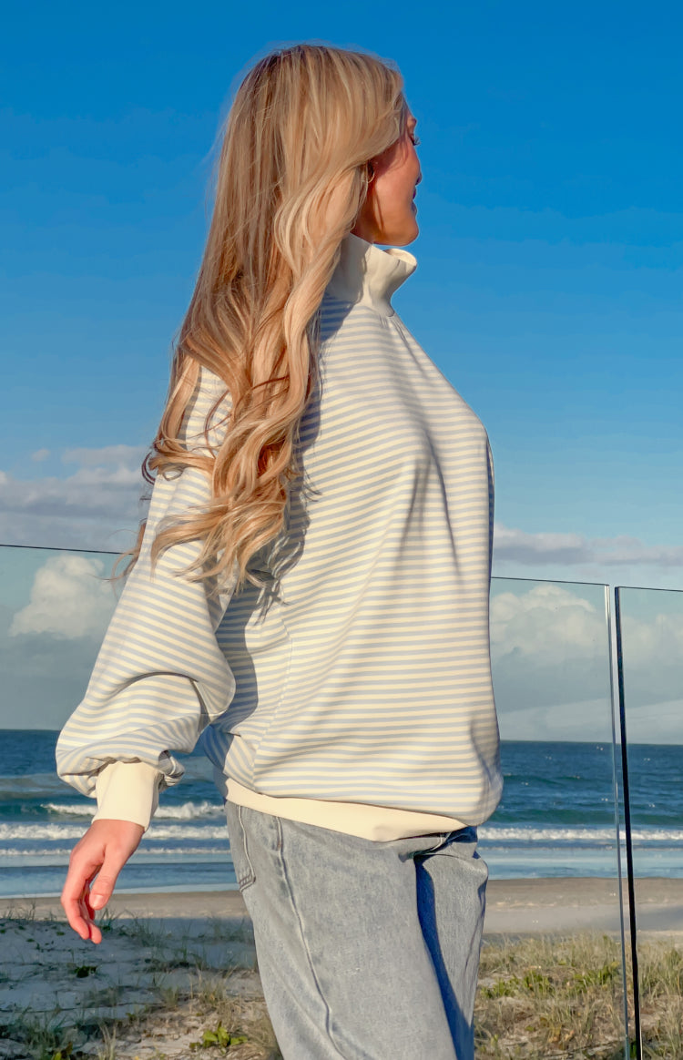 Side view of a blue and white striped mock neck sweater with long balloon sleeves and cream ribbed cuffs and hem