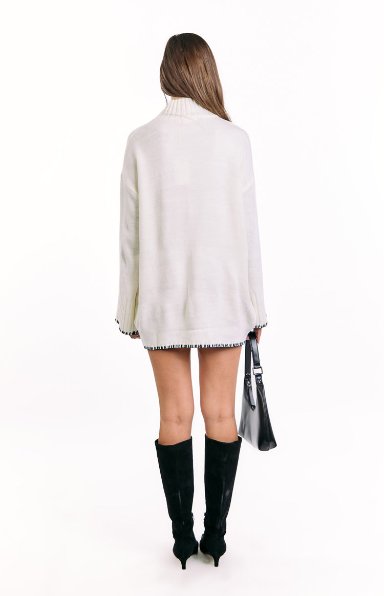 Rear view of a cream high neck sweater dress with black and white striped trim on the cuffs and hem