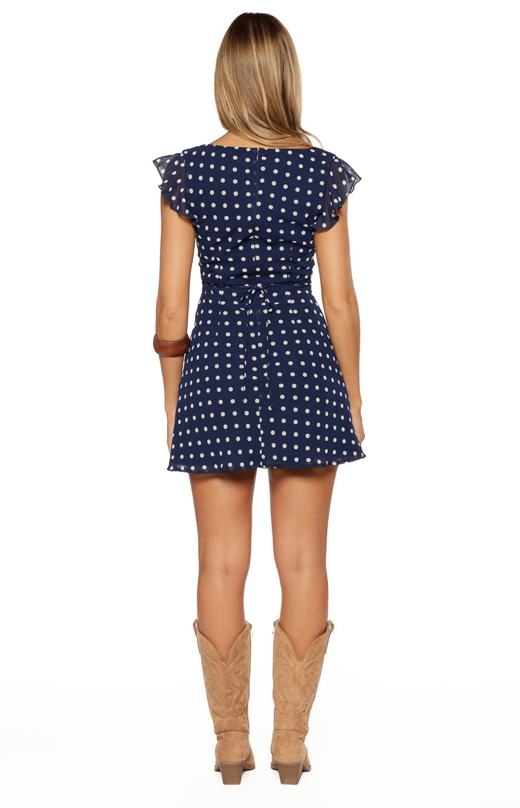 Rear view of a navy polka dot mini dress with a square back neckline, ruffled flutter sleeves, and a tie-back waist