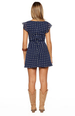 Rear view of a navy polka dot mini dress with a square back neckline, ruffled flutter sleeves, and a tie-back waist