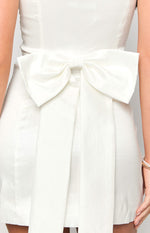 Rear view of a white mini dress showing a large bow detail at the back waist with long flowing streamers