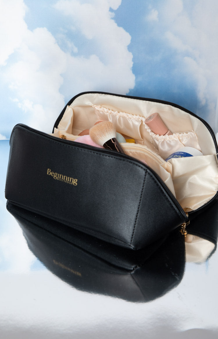 Open black cosmetic bag revealing cream satin interior lining with multiple elasticated pockets and gold zipper pull