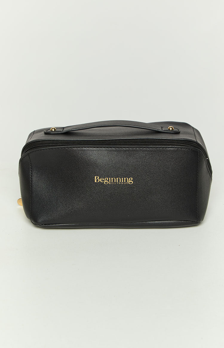 Elevated front view of a black cosmetic bag with a top handle, gold logo, and top zipper closure