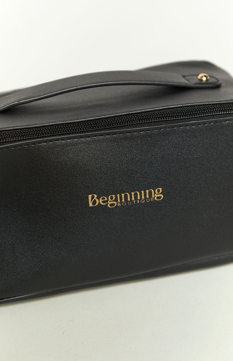 Close-up of the gold logo on the black textured faux leather, with a black zipper and top handle