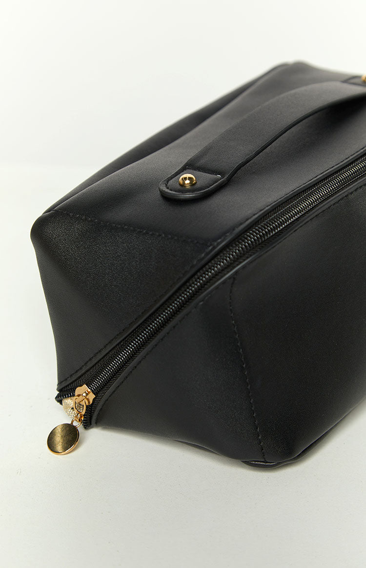 Close-up of the black cosmetic bag's gold zipper pull with a round charm and structured bottom corner