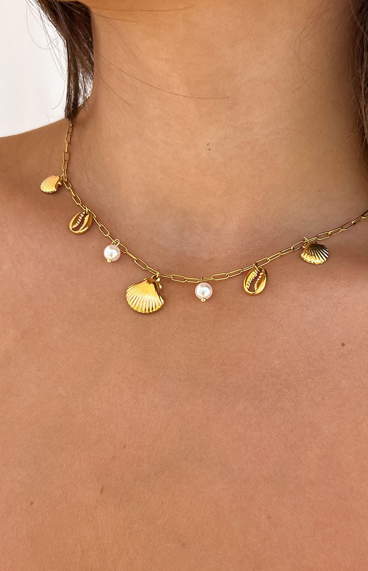 Detail shot of a gold necklace featuring diverse shell charms and delicate white pearls