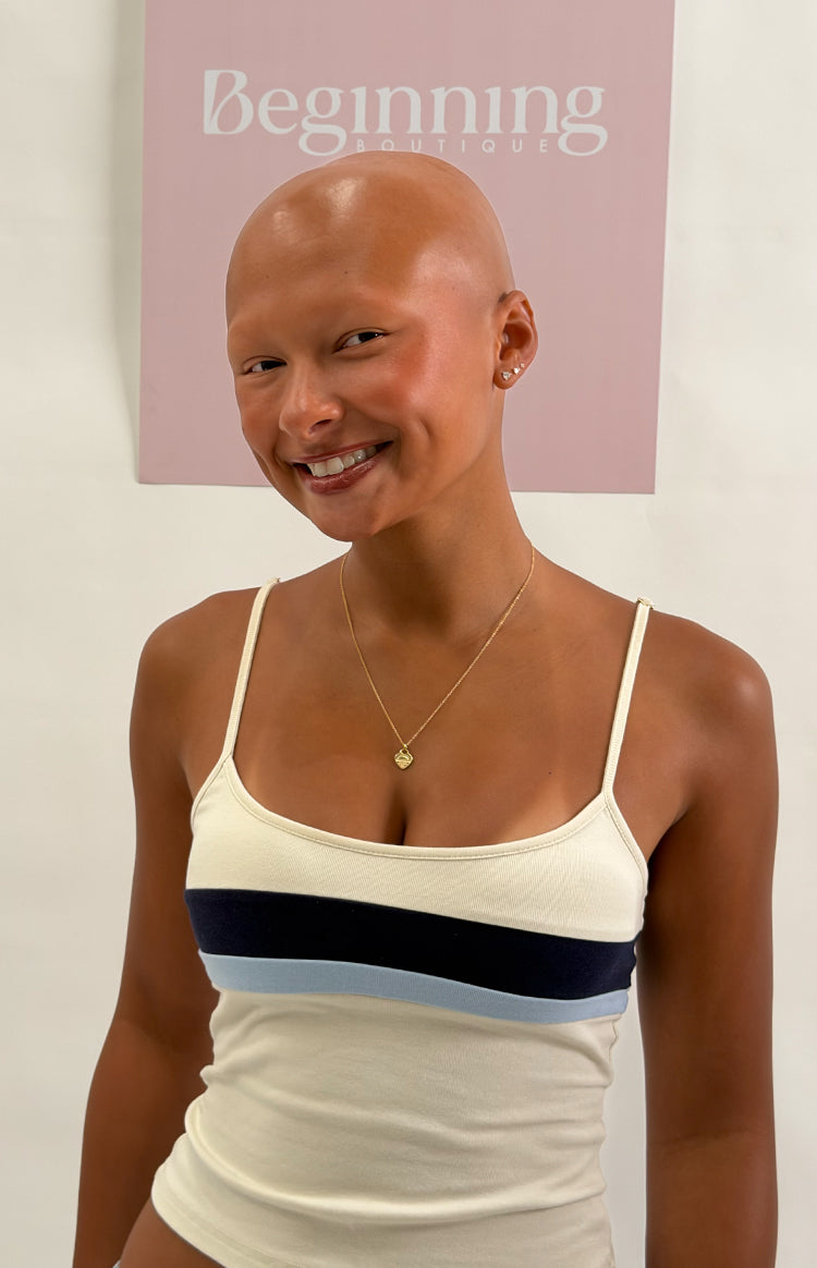 Close-up of a white ribbed knit singlet with a scoop neck and thin spaghetti straps, featuring navy and light blue chest stri