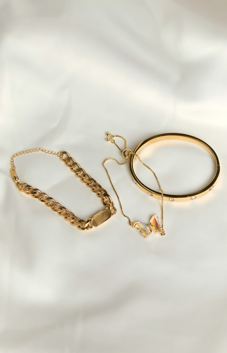 Three gold bracelets: a chunky chain with a brushed rectangular plate, a delicate chain with an iridescent butterfly, and a bangle with clear stones