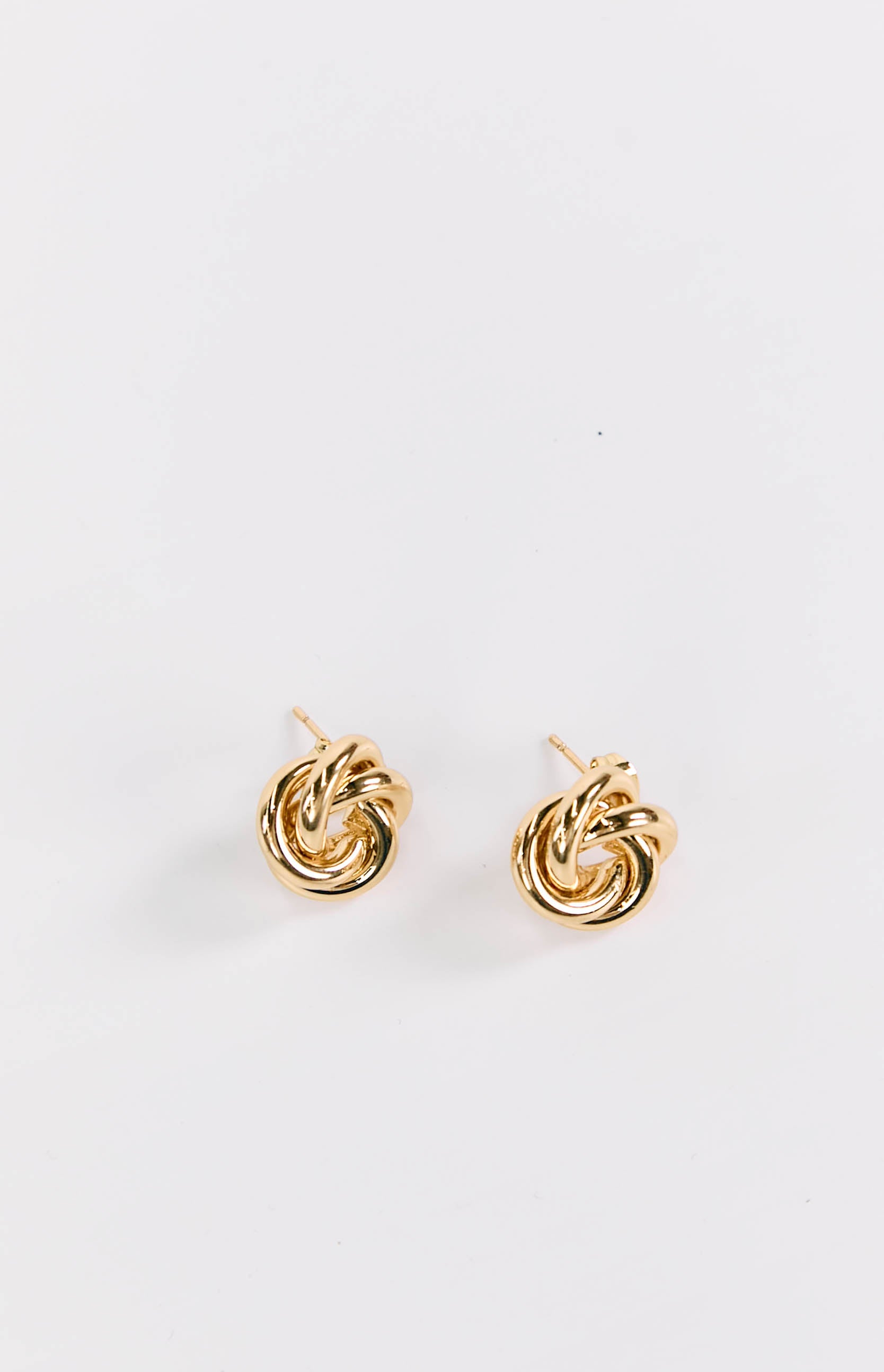 Two shiny gold knot stud earrings with the posts visible from a slightly elevated angle