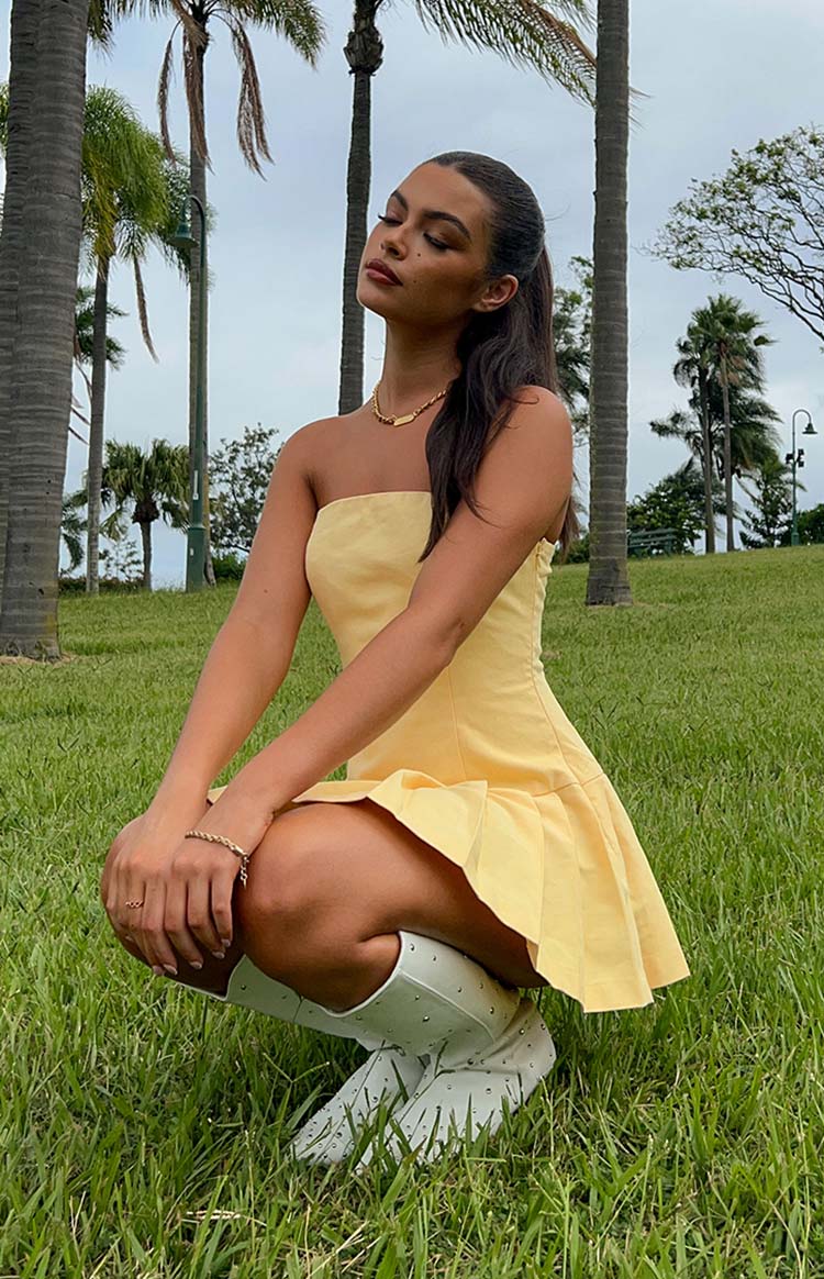 Side view of a yellow strapless mini dress with a fitted bodice and a pleated mini skirt