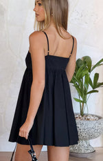 Side view of a black mini dress with thin adjustable spaghetti straps, a square back neckline, and a gathered A-line skirt