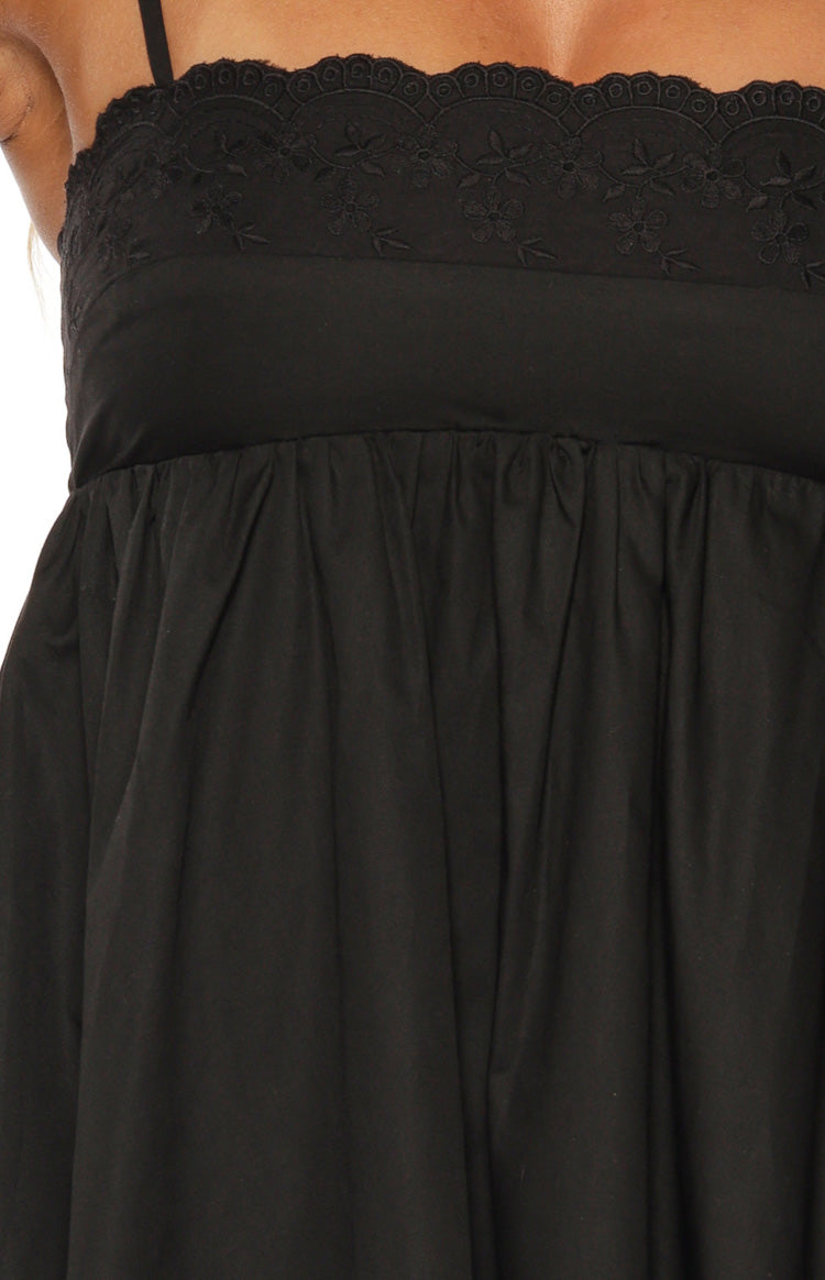 Close-up of the black mini dress showing eyelet embroidery and floral details on the bodice with a gathered empire waist