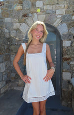 White mini dress with a square neckline, scalloped lace trim on straps, vertical textured fabric, and openwork hem