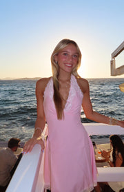 Baby pink mini dress with a deep V halter neckline and white lace trim along the neckline and hem