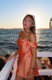 Side view of an orange satin off-the-shoulder mini dress with a draped neckline and flowy skirt