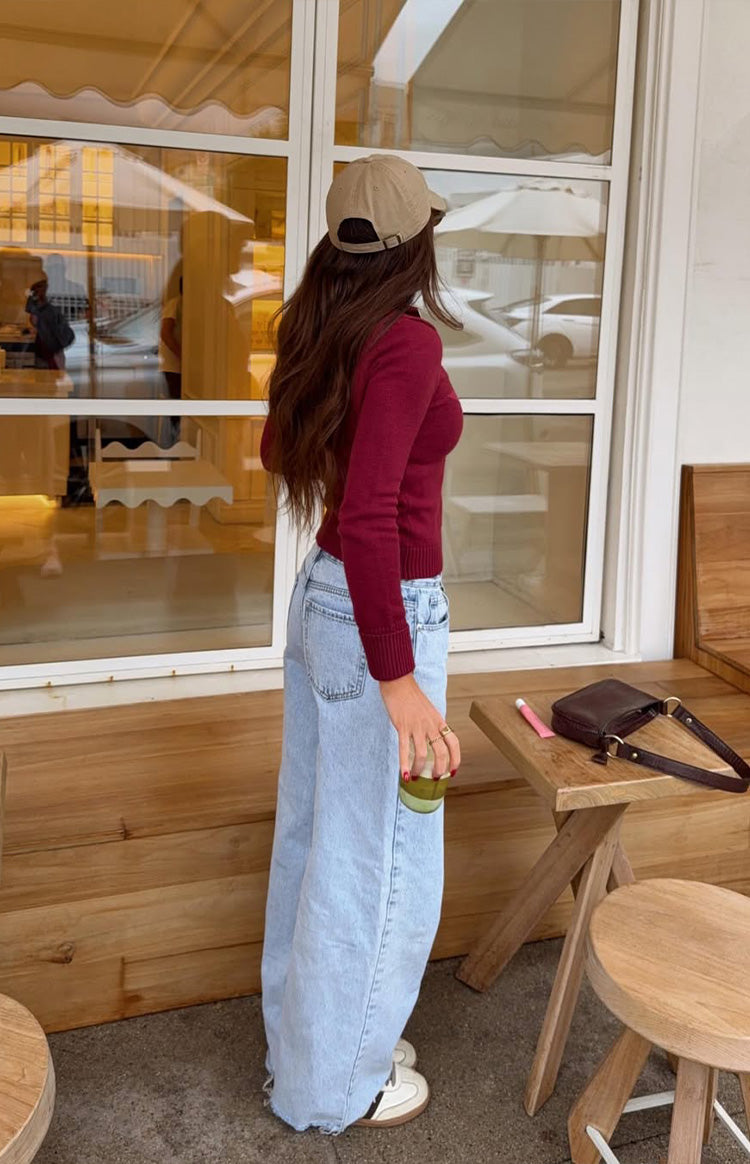 Side view of a fitted burgundy knit sweater with long sleeves, ribbed cuffs, and a ribbed hem