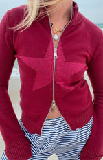 Close-up of the burgundy knit sweater with a darker star pattern and silver zipper unzipped from the bottom