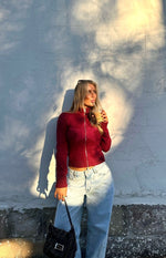 Front view of a burgundy knit sweater with a subtle star pattern, full silver zip, ribbed mock neck, and cropped hem