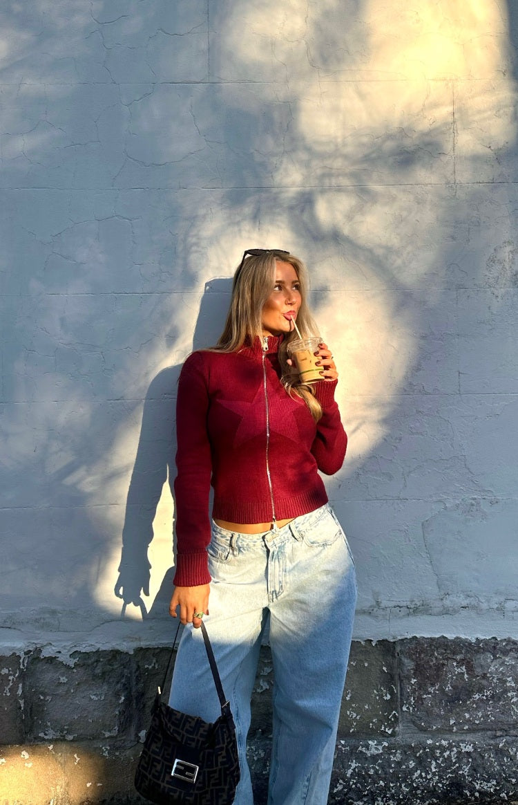 Front view of a burgundy knit sweater with a subtle star pattern, full silver zip, ribbed mock neck, and cropped hem