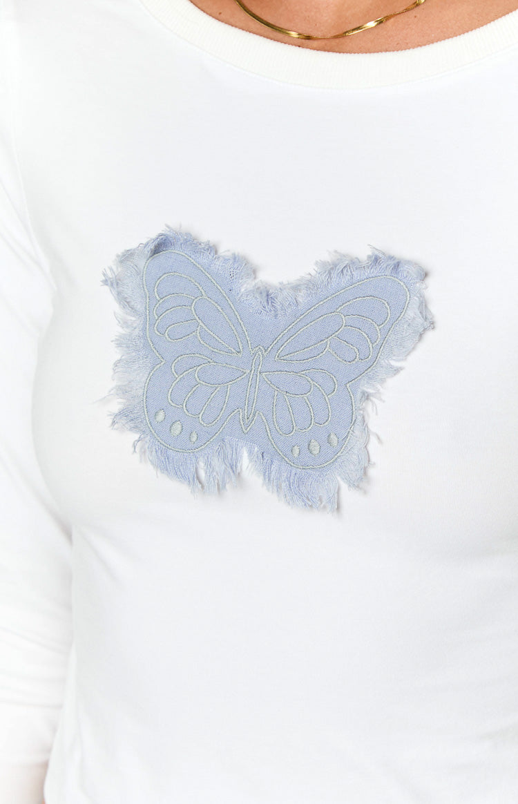 Close-up of the light blue butterfly appliqué with frayed edges on the front of the white long sleeve top