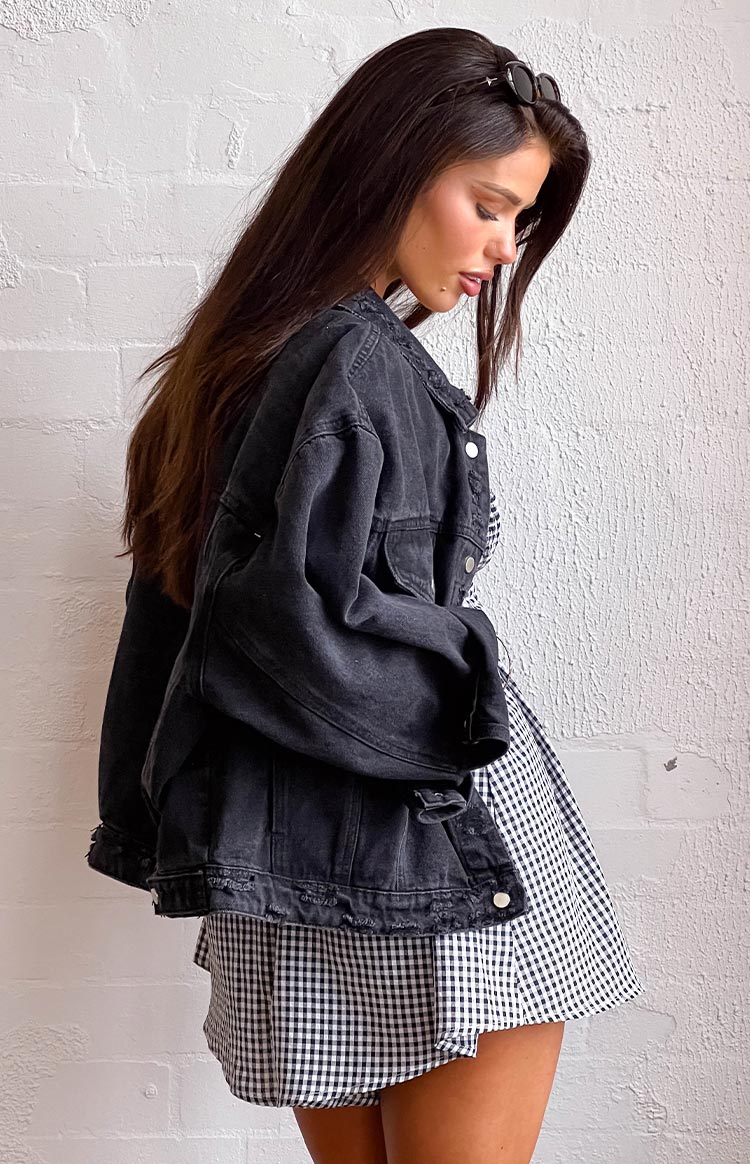 Side view of a washed black oversized denim jacket with distressed hem and collar