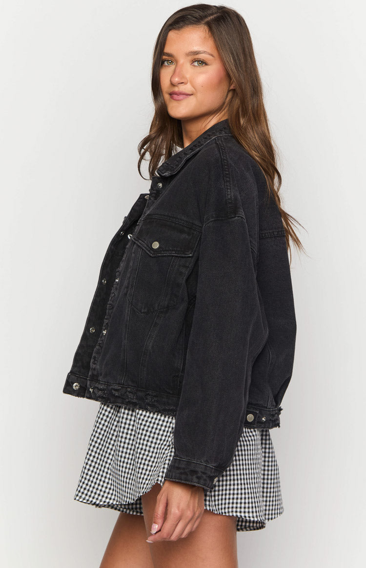 Side view of a black oversized denim jacket with a distressed raw hem and silver button details