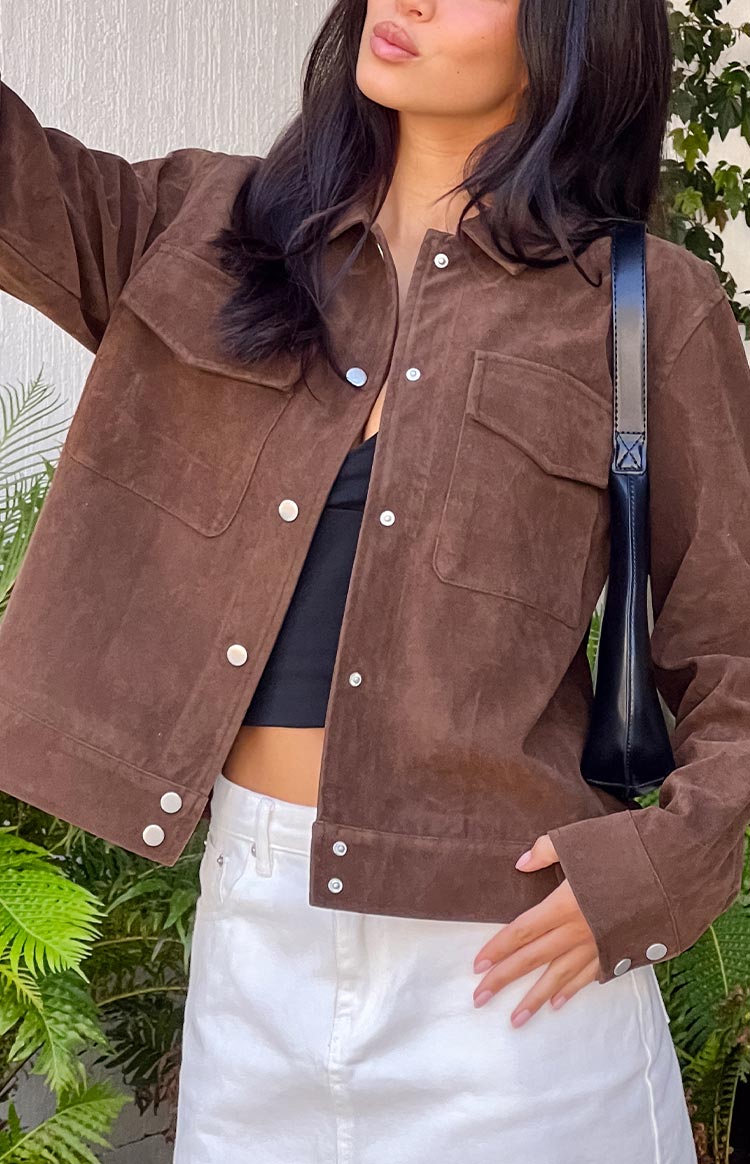 A short, brown suede-like jacket with a boxy fit, featuring a collar, two chest pockets, and silver snap buttons down the front. The jacket is worn open over a black crop top.