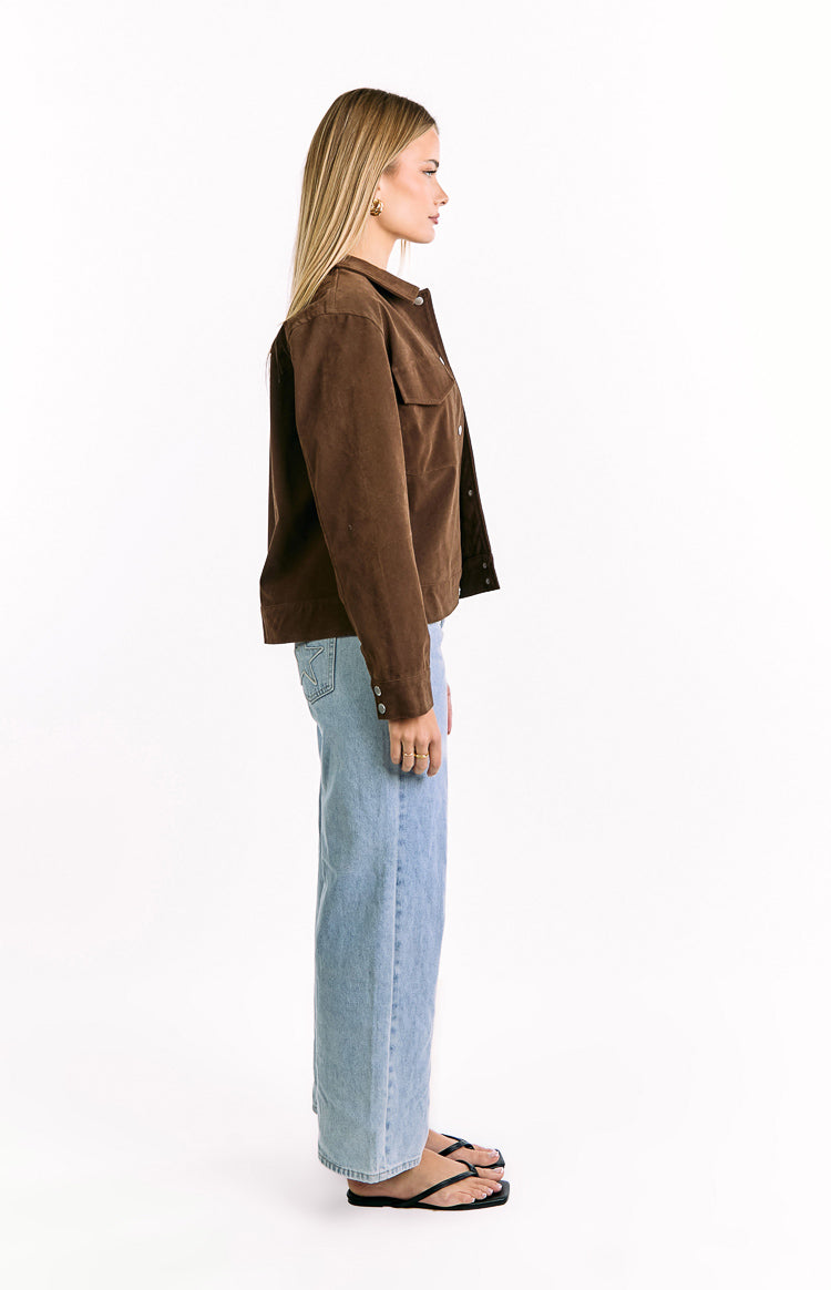Side view of a chocolate brown suedette jacket with a relaxed fit, long sleeves, and buttoned cuffs