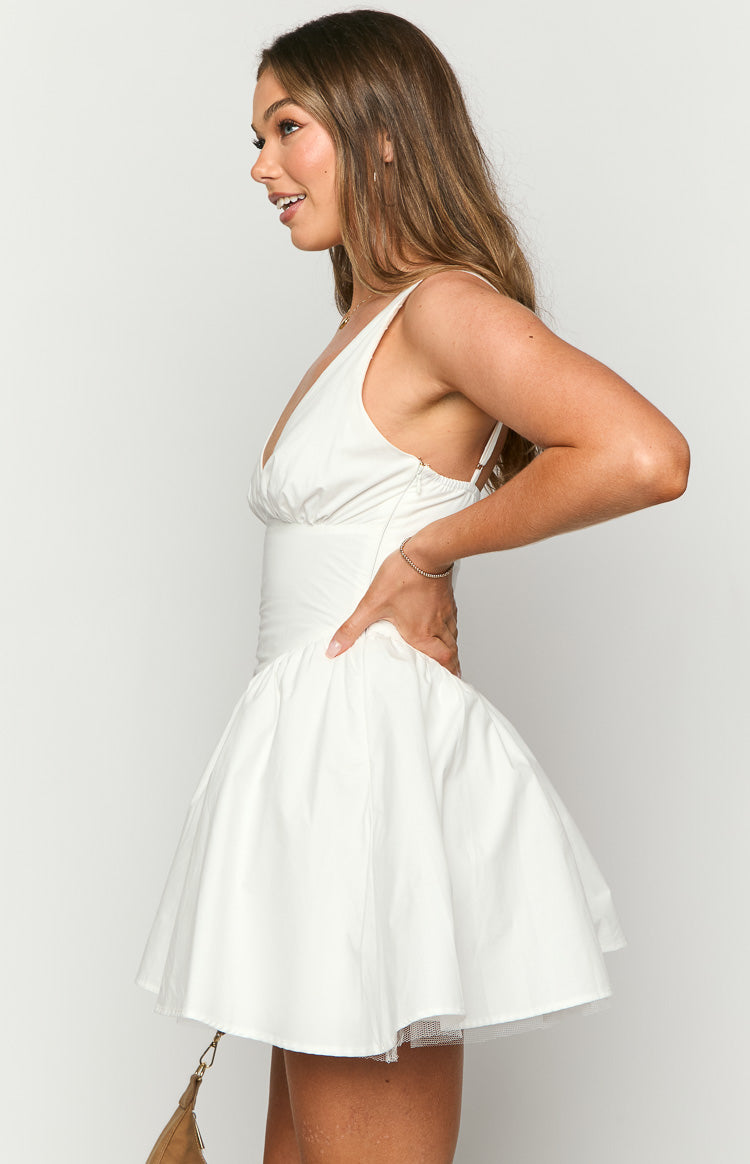 Side view of a white mini dress with a deep V-neck, ruched bust, fitted bodice, and a voluminous skirt with tulle underlay