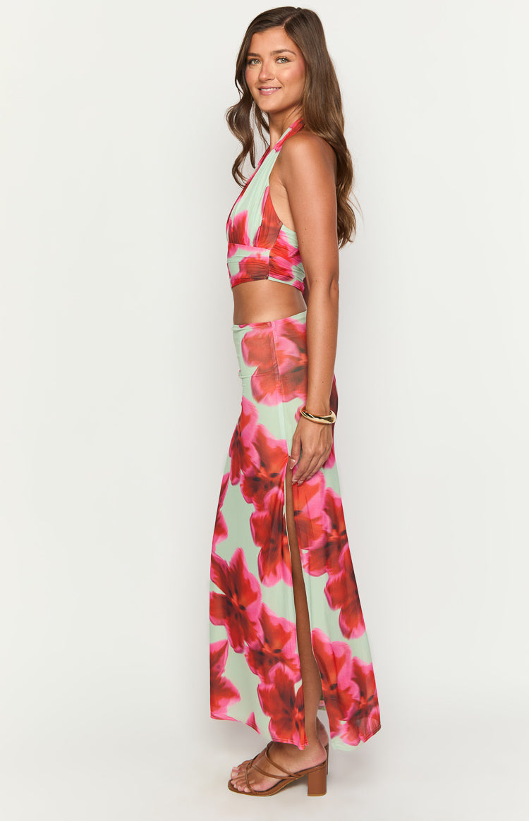 Side view of a green floral print maxi dress with a halter neckline, midriff cutout, and high side slit
