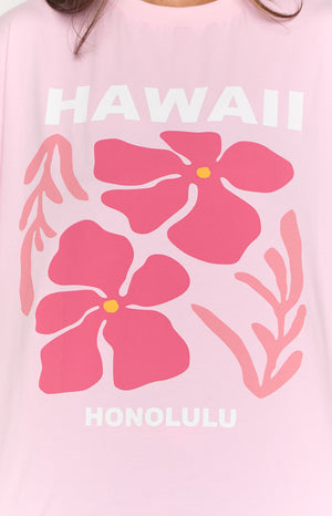 Close-up of the pink tee's graphic print featuring white 'HAWAII' and 'HONOLULU' text with two large pink flowers and leaves