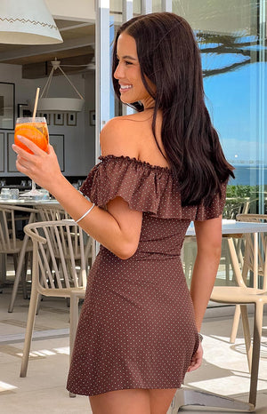 The side and back view of a brown polka dot off-the-shoulder mini-dress- featuring ruffled sleeves and a fitted waist- ideal for a casual summer day.