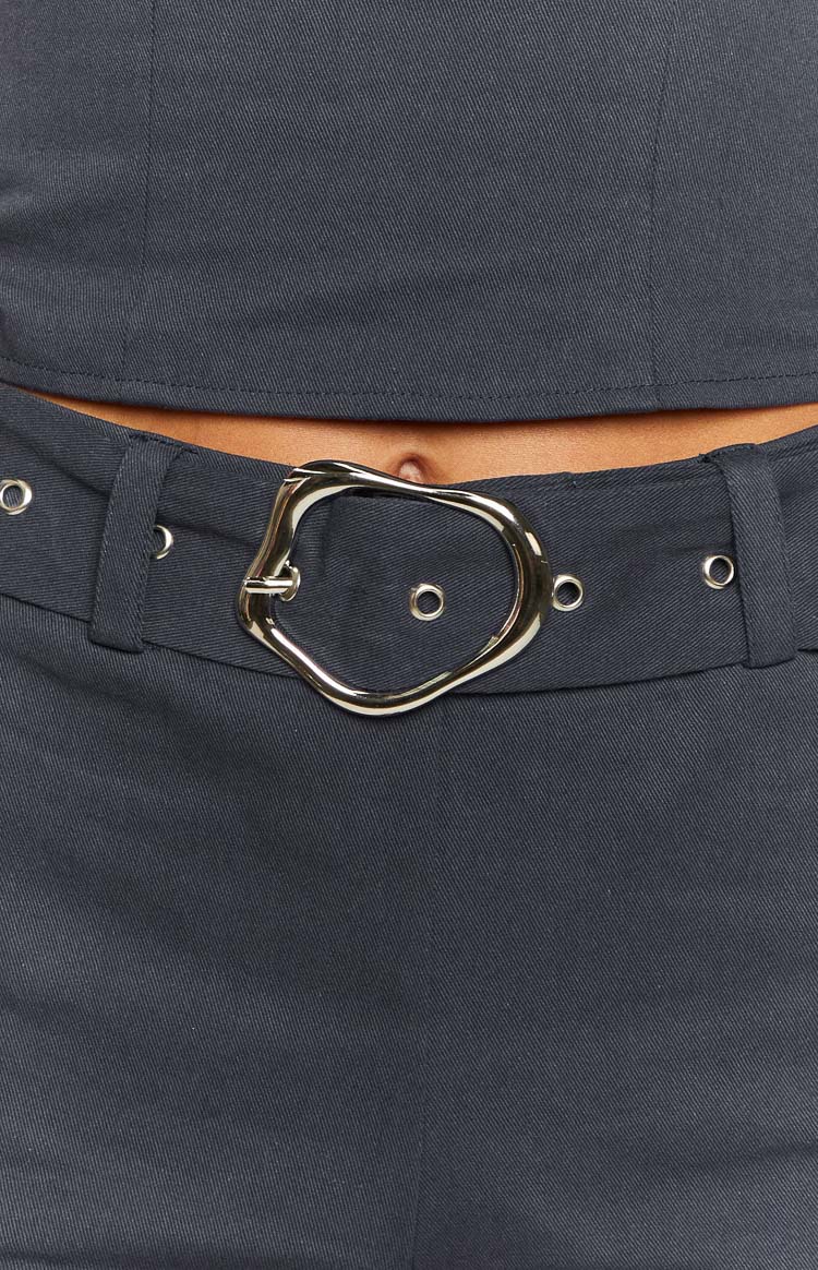 Close-up of the silver irregular buckle on the navy shorts belt with metal eyelets