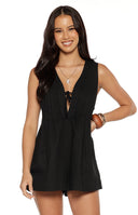 A lifestyle shot of our model wearing a short sleeveless black romper. This playsuit features a deep V-neckline with a keyhole opening that is secured at the top by a thin fabric tie. The bodice and flared shorts are accented with vertical pleated gathering.