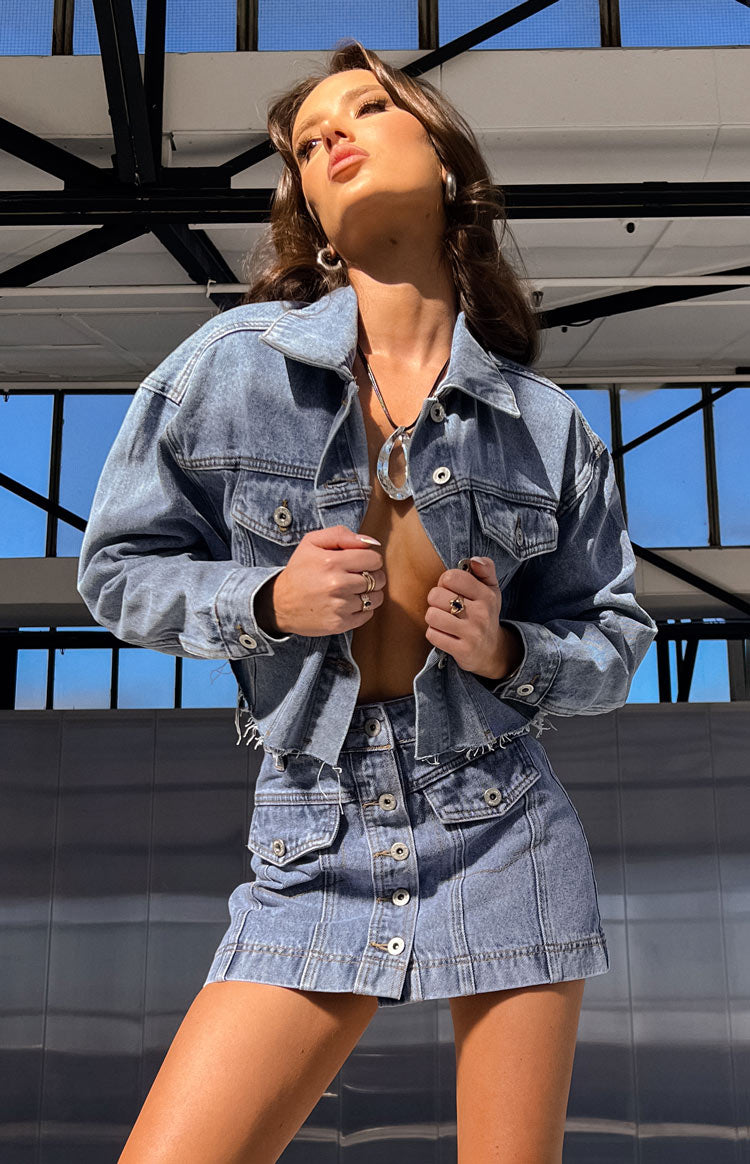 Front view of a mid-wash denim cargo mini skirt with a button-front closure and flap pockets